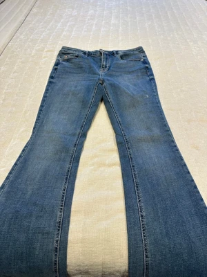 Blå bootcut jeans från Vero Moda - Säljer ett par klassiska blå bootcut jeans från Vero Moda. Jeansen har normal midja, fem fickor och snygga slitningar för en avslappnad look. Perfekta till sneakers eller boots och tillverkade i mjuk denim med lite stretch.