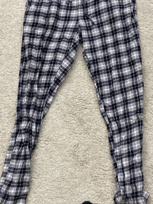 Rutiga pyjamasbyxor i svartvitt - Mysiga pyjamasbyxor med svartvitt rutmönster och dragsko i midjan. Tillverkade i mjukt tyg, perfekta för chillkvällar hemma. Klassisk rak passform och långa ben ger en avslappnad vibe. 