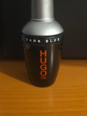 Hugo Boss Dark Blue parfym - En stilren parfymflaska från Hugo Boss, modell Dark Blue. Flaskan är mörkblå med silverfärgat lock och har märkets logga i orange text. Perfekt för dig som gillar klassiska och maskulina dofter.
