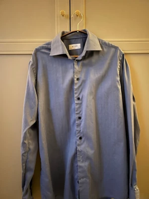 Blå skjorta från Eton slim fit - Snygg blå skjorta från Eton i slim fit-modell. Skjortan har klassisk krage, långa ärmar och knappar framtill. Tillverkad i mjuk bomull som känns skön mot huden. Perfekt för dig som gillar stilrena och tidlösa plagg.