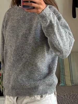 Grå stickad tröja i ullmix - Mysig grå stickad tröja med rund hals och ribbade muddar vid ärmslut och nederkant. Tröjan har en avslappnad passform och är tillverkad i en mjuk ullblandning som känns skön mot huden. Perfekt att slänga på sig när det är kyligt ute.