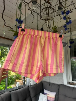 Randiga rosa och gula shorts - Säljer ett par färgglada shorts med breda rosa och gula ränder. De har en elastisk midja och är tillverkade i ett satin material. Perfekta till sommaren 