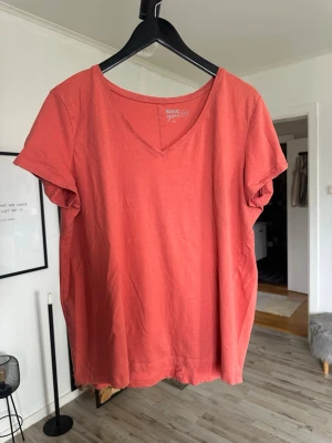 Korallröd t-shirt från Basic You - En enkel och snygg korallröd t-shirt från Basic You i ekologisk bomull. T-shirten har v-ringning och korta ärmar, perfekt för en avslappnad stil. Passformen är normal och materialet känns mjukt mot huden.
