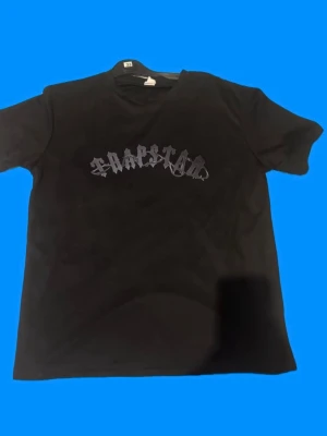 Svart t-shirt med tryck - Säljer en svart t-shirt med coolt tryck i gotisk stil på bröstet. T-shirten har korta ärmar och rund halsringning. Perfekt för dig som gillar streetwear och enkel stil.
