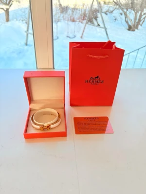 Vitt och guldigt armband  - Säljer ett exklusivt armband i vitt och guld. Armbandet har en elegant och stilren design med metall i guldfärg och vit emalj. Kommer i original ask och påse samt med äkthetskort. Perfekt accessoar för dig som gillar lyxiga detaljer.