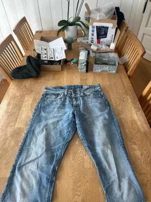 Blå raka jeans från Nudie Jeans - Säljer ett par klassiska blå jeans från g-star med raka ben och snyggt slitna detaljer. Jeansen har fem fickor, normal midja och är gjorda i bomull. Perfekta för en avslappnad och trendig stil.