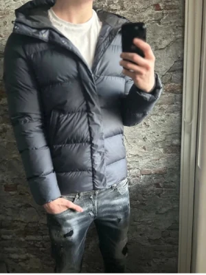 J.Lindeberg puffer Jacka - Säljer en mörkblå pufferjacka från j.lindeberg med stor huva och dragkedja framtill. Jackan har en klassisk quiltad design, två sidofickor och är tillverkad i ett glansigt material som ger en modern look. Perfekt för kalla vinterdagar. PS nypris :- c.a 4000kr, ja säljer den för endast 1199 utan defekter. 🤩😁