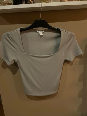 Grå croppad topp från Amisu - Snygg grå croppad topp  med fyrkantig ringning och korta ärmar. Perfekt att styla med höga jeans eller kjol. Enkel och stilren design som passar till många olika looks.