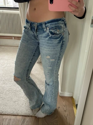 Ljusblå slitna bootcut jeans True Religion - Bootcut low waist jeans från TRUE RELIGION. Slitningar och hål på benen med fina fickor. Fint Storlek 25 men passar även mig som har lite större. Lite slitna längst ner på benet💕