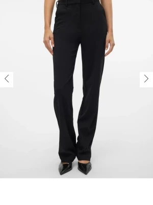 Svarta kostymbyxor från vero Moda  - Stilrena svarta kostymbyxor från vero Moda  med raka ben och hög midja. Byxorna har hällor för skärp, diskreta sidofickor och stängs med dragkedja och hake. Perfekta för en clean och trendig look.
