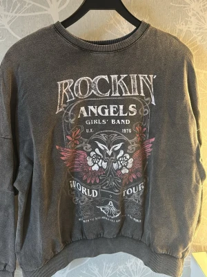 Grå sweatshirt  - Urtvättad-Grå sweatshirt med tryck framtill. Tröjan har rund halsringning, ribbade muddar och en vintageinspirerad design med text och grafiska detaljer i vitt, rosa och rött. Storlekslappen är borta men passar definitivt mellan S-M