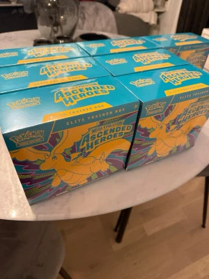 Pokémon Ascended Heroes Elite Trainer Box - Säljer flera Pokémon Mega Evolution Ascended Heroes Elite Trainer Box. Lådorna är turkosa med färgglad design och motiv av Dragonite. Perfekt för samlare eller Pokémon-fans som vill utöka sin kortsamling.