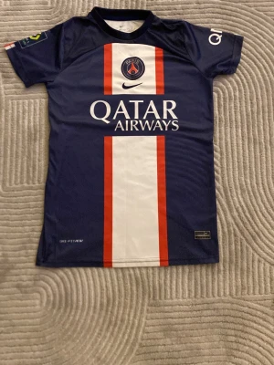 PSG Neymar Jr matchtröja blå - Snygg PSG matchtröja i blått med vita och röda detaljer, Neymar Jr och nummer 10 på ryggen. Tillverkad i lätt och ventilerande material, perfekt för fotboll eller träning. Qatar Airways och Ooredoo-loggor tryckta på framsidan och baksidan.