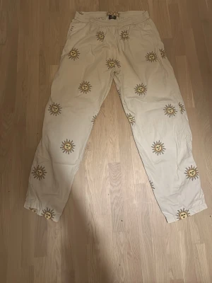 Beige byxor med soltryck från Sweet sktbs  - Unika beige byxor från sweet sktbs med elastisk midja och soltryck över hela byxorna.