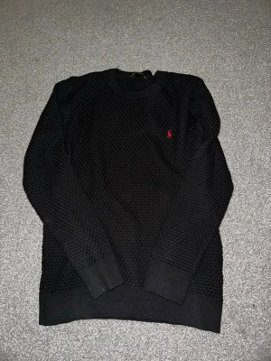 Svart stickad tröja från Ralph Lauren - Svart stickad tröja från Ralph Lauren med klassiskt röd broderad logga på bröstet. Passar storlek S och M. Tröjan har rund halsringning, ribbade muddar och en grovstickad struktur som ger en cool och tidlös look. Skriv över det minsta lilla eller över den minsta funderingen!🔥🔥