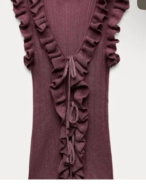 Lila ribbad topp med volang och knyt - Supersöt lila ribbad topp med djup v-ringning, volangdetaljer längs ringningen och knyt framtill. Ärmlös och croppad modell som ger en trendig look. Perfekt att styla med både jeans och kjol för en cool vibe.