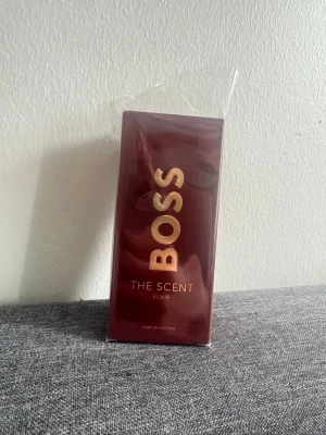 BOSS The Scent Elixir Parfym - BOSS The Scent Elixir är en intensiv parfym med elegant mörkröd förpackning och flaskan har en unik, mångkantig form. Guldtexten på kartongen ger en lyxig känsla. Perfekt för dig som vill ha en kraftfull och exklusiv doft, helt oanvänd.