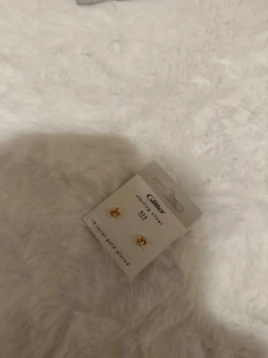 Guldpläterade knutörhängen från Glitter - Snygga små örhängen i form av en knut från Glitter. Örhängena är guldpläterade och tillverkade i sterlingsilver, vilket gör dem både stilrena och trendiga. Perfekta för att ge din look en elegant touch.