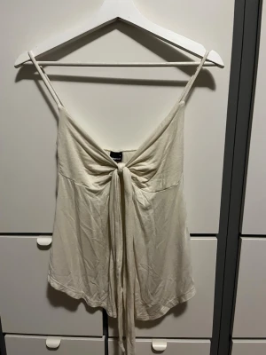 Beige linnetopp med knyt fram från ginatricot - Supersöt beige linnetopp med smala axelband och snygg knytning framtill. Perfekt för varma dagar och enkel att styla med jeans eller kjol. Luftigt material som känns skönt mot huden. 