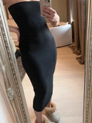 Svart tubklänning i midilängd - Säljer en svart, tight tubklänning i midilängd. Klänningen är axelbandslös och har en kroppsnära passform som framhäver siluetten. Perfekt för dig som gillar en stilren och enkel look. Materialet är stretchigt och följsamt.