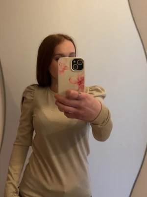 Beige tröja med puffärm - Säljer en beige långärmad tröja med puffade axlar och ribbade muddar. Tröjan har en slim fit och är gjord i ett mjukt och stretchigt material . 