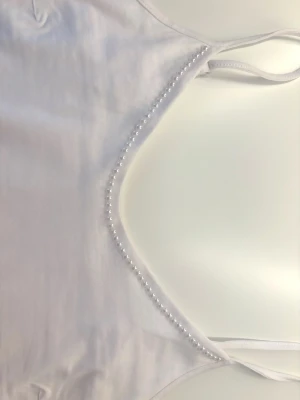 Vit linnetopp med pärldetaljer - Vitt linne med pärlor runt urringningen (går även att köpa med diamanter runt urringningen). Perfekt nu till sommaren. Enkel och stilren design som passar till många outfits. Finns i alla storlekar (Tvätta helst i 30 grader)