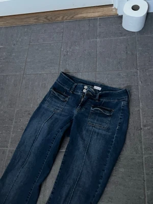 Mörkblå bootcut jeans med fickor - Säljer ett par mörkblå bootcut jeans med dubbla framfickor och markerade sömmar längs benen. Jeansen har låg midja och är supersnygga. Säljer pga att dom är för korta på mig som är 176! Superfint material!