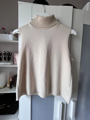 Beige stickad ärmlös polotröja Zara - Säljer en beige stickad ärmlös polotröja från Zara. Tröjan har en hög ribbad polokrage och är gjord i mjukt stickat material.
