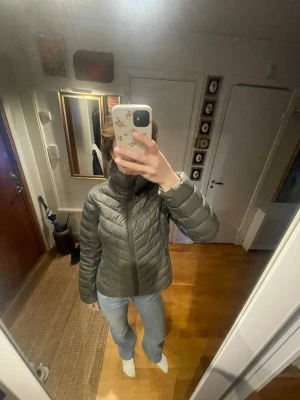 Grön dunjacka - Säljer en grön dunjacka med huva och dragkedja framtill. Jackan har quiltad design och hög krage, samt två fickor! 