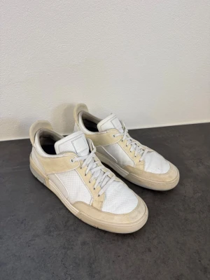 Vita sneakers från Jacob Cohen - Stilrena vita sneakers från Jacob Cohen med beige mockadetaljer och vit mesh. Klassisk låg modell med vita snören och gummisula. Perfekta för dig som gillar en clean och sportig look.