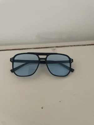 ”Grisch” glasögon - Snygga solglasögon med svart pilotformad båge och ljusblå tonade glas. Klassisk design som ger en cool vibe till din outfit. Perfekta för soliga dagar och trendiga looks. Pris går att diskuteras