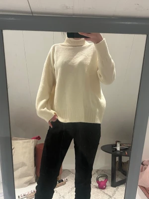 Krämvit polotröja i stickat - Mysig krämvit stickad polotröja med avslappnad passform och breda ribbade muddar. Tröjan har hög polokrage och långa ärmar. Perfekt för lager på lager och enkel att matcha till olika outfits.