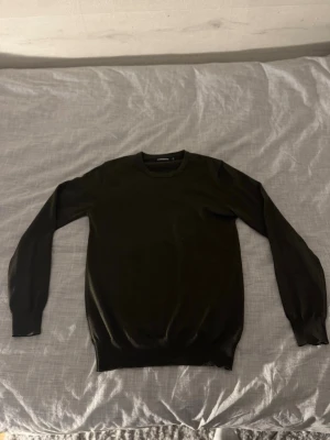 Svart stickad tröja med rund hals - En enkel och stilren svart stickad tröja med rund halsringning och långa ärmar. Tröjan har ribbade muddar vid ärmslut och nederkant, vilket ger en snygg passform. Perfekt basplagg för lager på lager och funkar till det mesta.