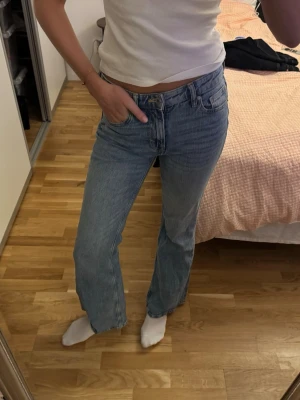 Blå raka jeans med hög midja - Säljer ett par klassiska blå jeans med rak passform och hög midja. Jeansen har fem fickor, gylf med dragkedja och knapp samt en snygg tvättad look. Perfekta för en avslappnad stil och lätta att matcha med olika toppar.