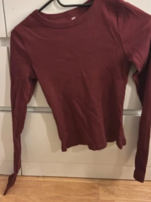 Mörkröd långärmad topp - En enkel och stilren mörkröd långärmad topp med rund halsringning. Toppen har en slim passform och är perfekt att matcha med jeans eller kjol. Tillverkad i mjukt material som känns skönt mot huden.