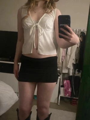 Vit croppad linnetopp med knyt - Snygg vit croppad linnetopp med knyt framtill och djup v-ringning. Toppen är ärmlös och har en lätt och luftig känsla, perfekt för varma dagar. Enkel men trendig design som passar till många olika outfits.