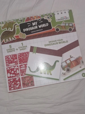 Pysselbok - Säljer ett ritportfolio-set 'My Dinosaur World' från Crelando. Innehåller 5 schablonark (stensiler) och 1 klistermärkesark med dinosaurietema utöver alla sidor med dinosauriefigurer samt bil. Perfekt för att designa din egen dinosaurievärld. Spiralbunden bok i grönt, vitt och rött med illustrationer av dinosaurier och fordon. Dragits ur 2 sidor, annars inga defekter!
