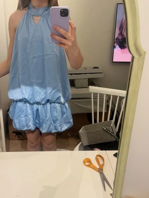 Ljusblå omlottklänning med volang - Säljer en ljusblå kort klänning med halterneck och liten öppning vid halsen. Klänningen har volangdetaljer och en lös passform som är avslappnad och snygg!! Den är helt ny utan prislapp. varumärket är shein!!❤️
