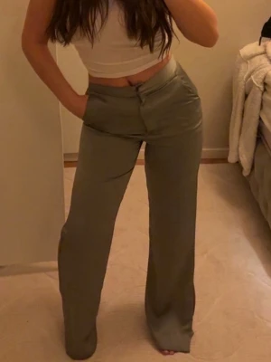 Olivgröna vida leggings - Snygga olivgröna satinbyxor i kostymmodell som ger en elegant och stilren look. Tyget har en mjuk, lätt glansig finish som gör dem både bekväma att bära och extra fina till både vardag och fest. Byxorna är endast använda några få gånger och är i mycket fint skick. Säljs eftersom de tyvärr är lite för långa för mig (jag är 157 cm).