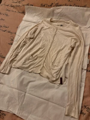 Beige tunn kofta med knappar - Säljer en tunn och mjuk beige kofta med rund halsringning och knäppning framtill. Koftan har två små fickor fram och långa ärmar. Perfekt att slänga över en topp för en enkel och clean look.