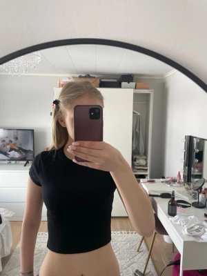 Svart croppad topp från H&M Divided - Svart, croppad topp från H&M Divided med ribbad struktur och korta ärmar. Enkel och stilren design som passar perfekt till jeans eller kjol. Materialet är mjukt och stretchigt, vilket gör den bekväm att bära hela dagen.