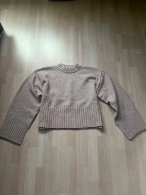 Ljusrosa stickad tröja från Monki - Trendig ljusrosa stickad tröja från Monki med croppad passform. Tröjan har bred ribbstickad kant nedtill och vid ärmsluten samt rund halsringning. Perfekt att styla med höga jeans för en avslappnad look. Har aldrig använt den.