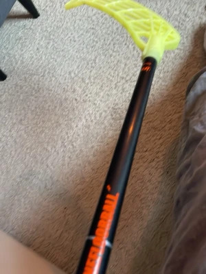 Zone innebandyklubba  - Säljer en innebandyklubba från Unihoc med svart skaft och neongult blad. Klubban har tryckt logga i orange på skaftet och bladet är tillverkat i plast med ett öppet rutmönster. Perfekt för dig som gillar innebandy och vill ha en snygg klubba.