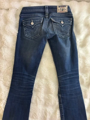True Religion blå bootcut jeans - Supersnygga blå bootcut jeans från True Religion med lite slitningar slitningar och ett hål på höger ben. Bortsett från det är de i jätte fint skick. 💞