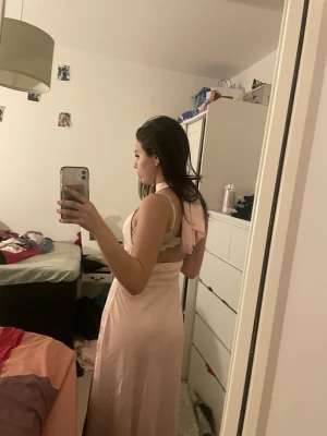 Ljusrosa  balklänningmed slits - Säljer en elegant ljusrosabalklänning soch ärmlös design. Klänningen har en snygg omlott-detalj i ryggen och ett mjukt, flowigt material som ger en fin siluett. Perfekt för dig som vill ha en stilren och feminin look. Den är aldrig använd köptes för min bal men vill köpa ny och därför säljer jag den. Prislappen är fortfarande på. Pris går att diskutera. Men den köptes för 500 kr.