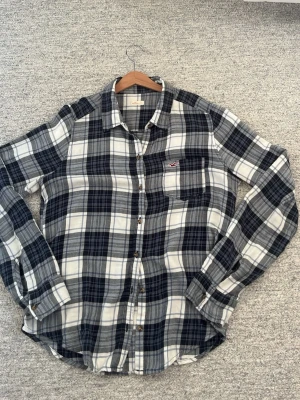 Rutig skjorta från Hollister - Snygg rutig skjorta från Hollister i blått, vitt och grått. Skjortan har klassisk krage, bröstficka med broderad logga och knappar framtill. Tillverkad i mjuk bomull och har långa ärmar. Perfekt för en avslappnad och trendig look. Står small men sitter som xs