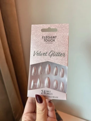 Elegant Touch Velvet Glitter lösnaglar - Säljer ett set med 24 lösnaglar från Elegant Touch i modellen Velvet Glitter. Naglarna har en skimrande, ljusrosa färg med glittereffekt och en elegant, mandelformad design. Lim medföljer i förpackningen.