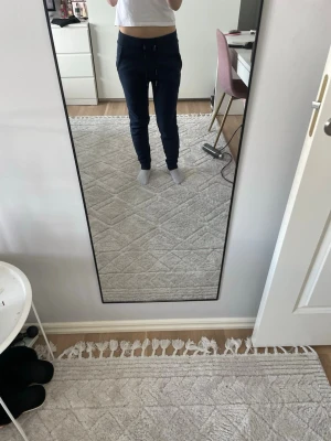 Mörkblå mjukisbyxor med dragsko - Säljer ett par mörkblå mjukisbyxor med smal passform och dragsko i midjan. Byxorna har resår vid bensluten och sidofickor. Perfekta för chill dagar hemma eller när du vill vara bekväm men ändå se snygg ut.