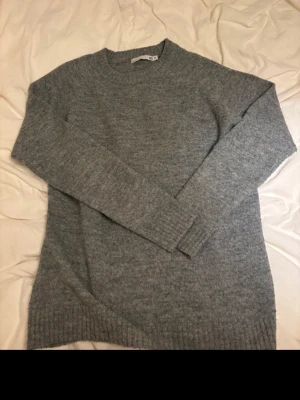 Grå stickad tröja från 157 - Mysig grå stickad tröja från 157 med rund halsringning och ribbade muddar vid ärmslut och nederkant. Perfekt för lager på lager och enkel att matcha med olika outfits. Klassisk modell i mjukt material.