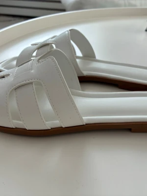 Vita sandaler stl 38 Nya - Ett par vita sandaler med en öppen tå och en platt sula. Sulorna är bruna med en lätt textur för grepp. New Yorker stl 38. Nya.